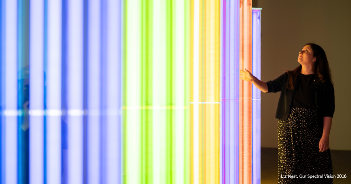 Woman stodd next to a colourful light artwork inside the Light Durham.